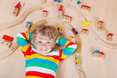Adorable blond child playing wooden trains and roalroad indoor. Active kid boy wearing colorful shirt and having fun with building and creating.